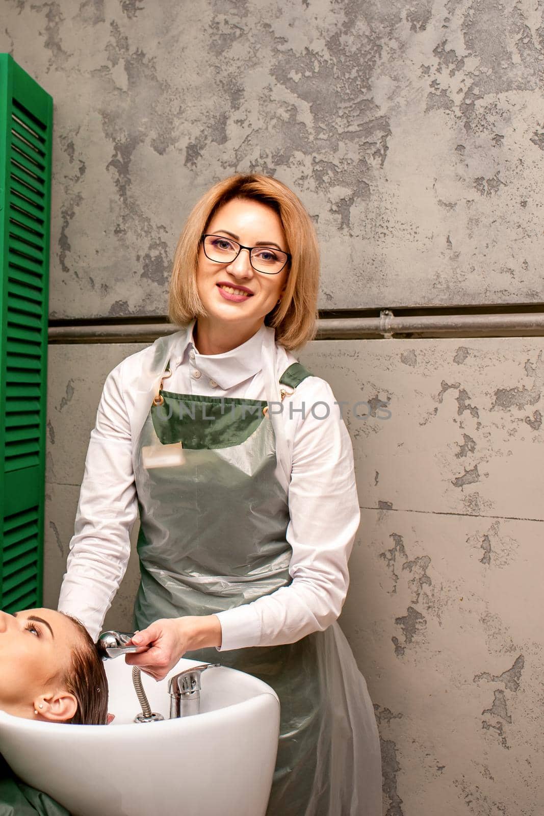 Portrait of female hairdresser washing hair of the young caucasian woman in a beauty salon