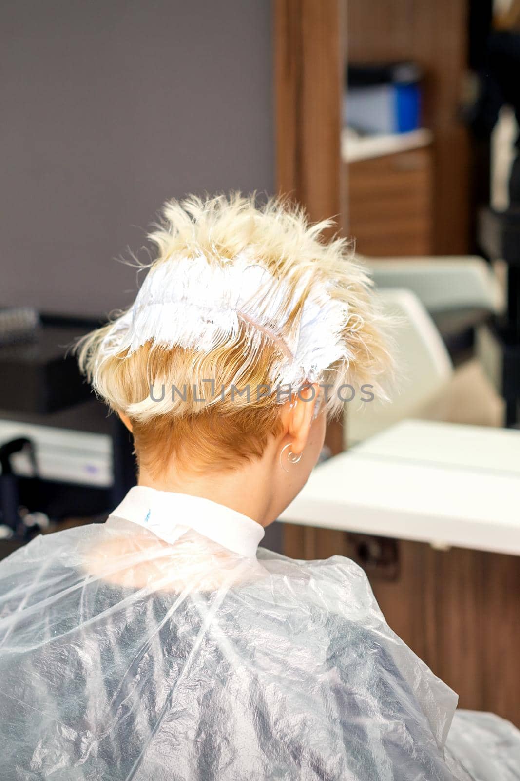 Coloring white hair with hair dye of the young caucasian blonde woman sitting at a hair salon, close up