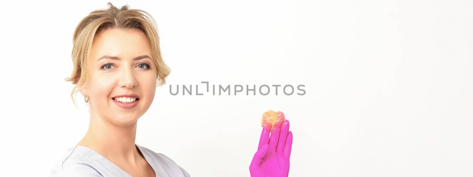 Young caucasian smiling female beautician holding wax for depilation over white background. Yellow sugar paste in hands master of depilation. Epilation concept. by okskukuruza