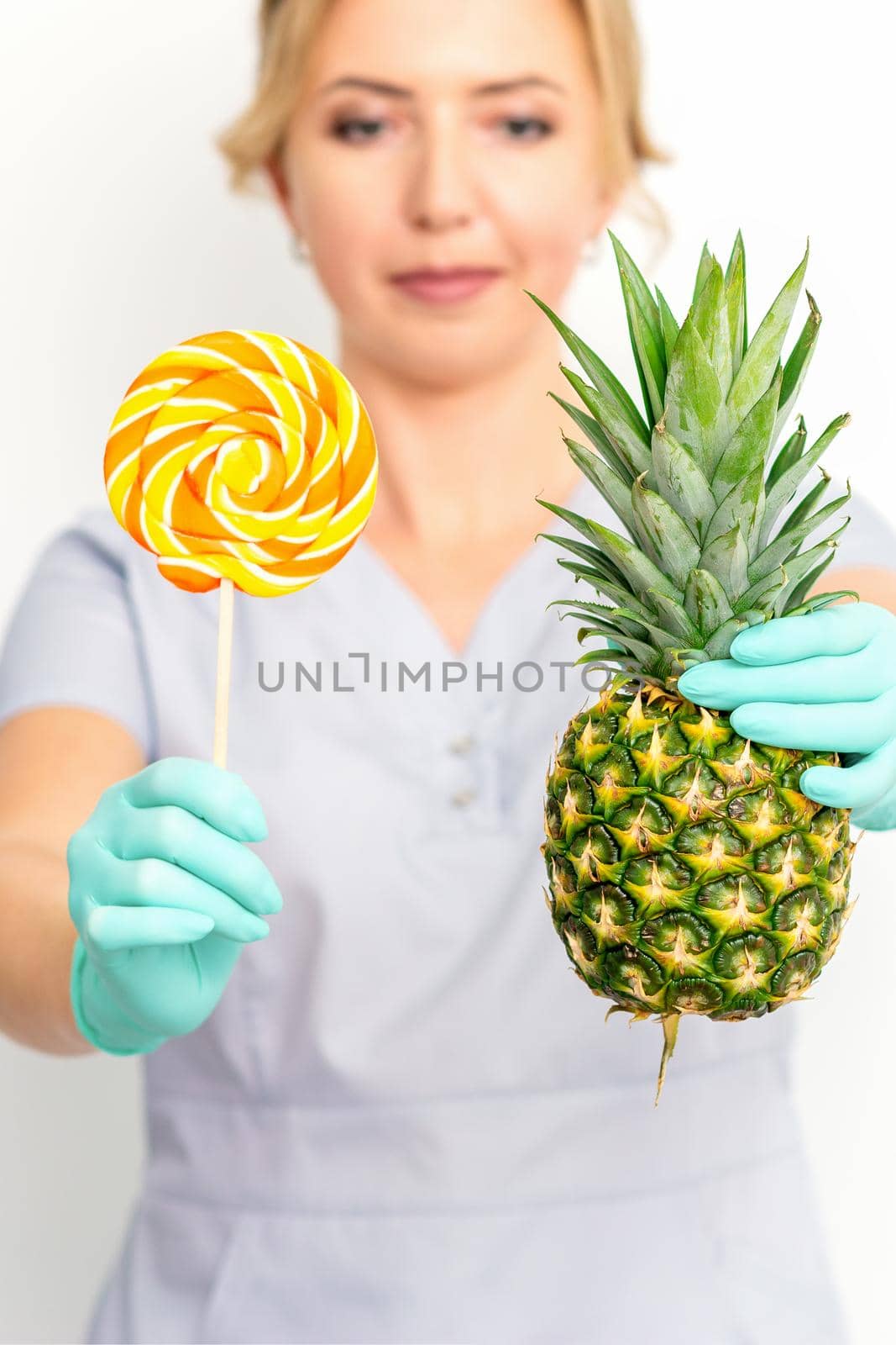 Young caucasian female doctor nutritionist holding fresh pineapple with lollipop over white background