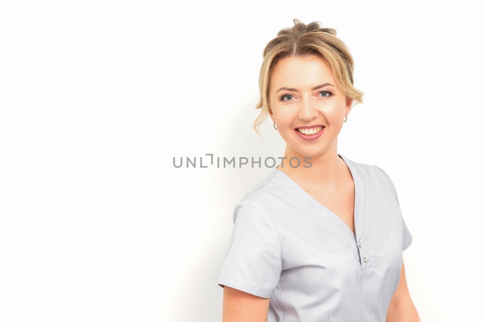 Close-up portrait of young smiling female caucasian healthcare worker standing staring at the camera on white background