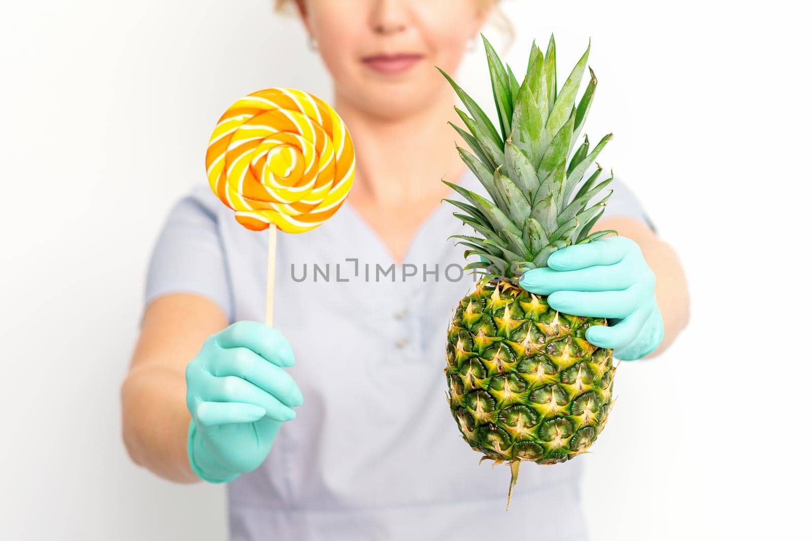 Young caucasian female doctor nutritionist holding fresh pineapple with lollipop over white background