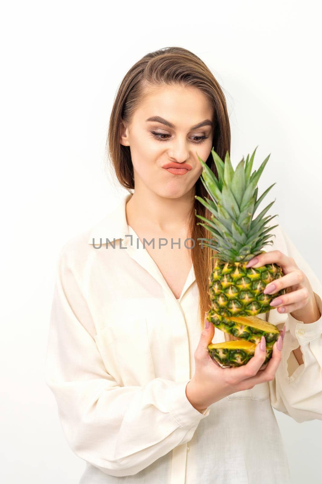 Beautiful young Caucasian woman holding pineapple and disappointed looking wearing a white shirt over white background