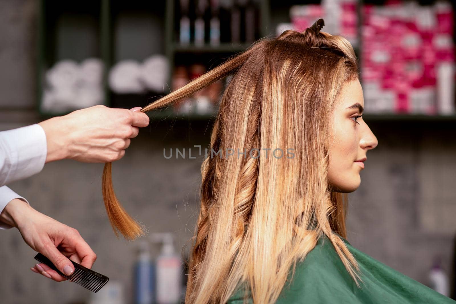 Professional hair care. Beautiful young caucasian blonde woman with long hair receiving hairstyling in a beauty salon
