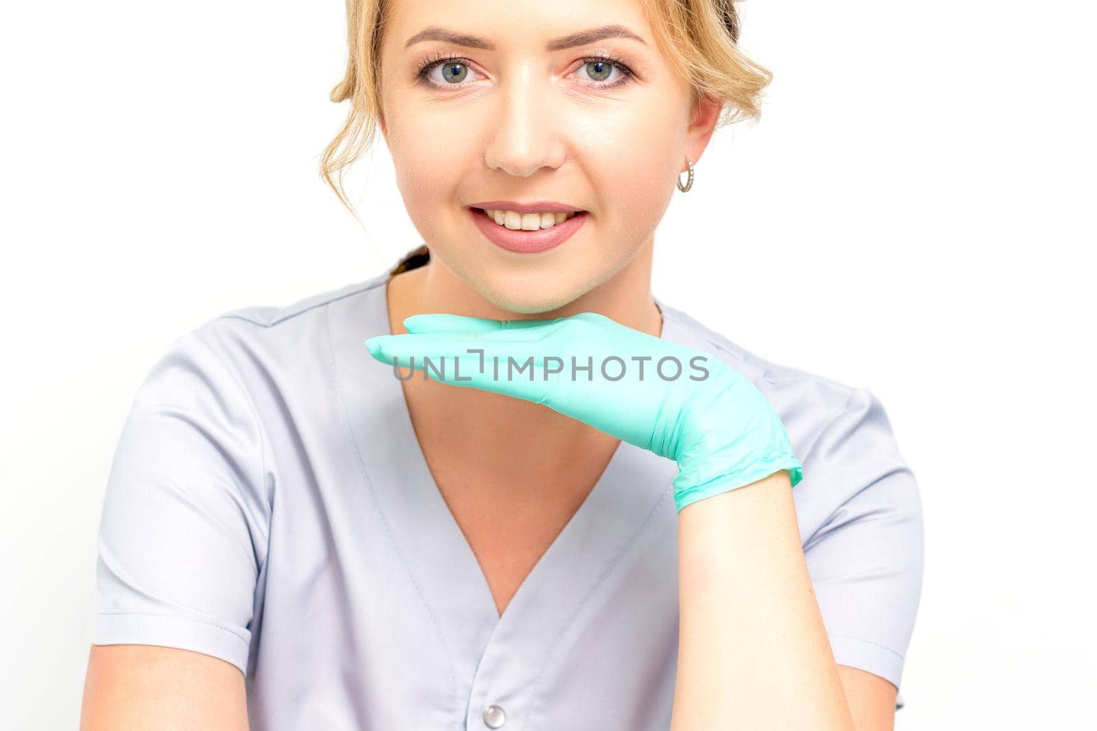 Close-up portrait of young smiling female caucasian healthcare worker standing and staring at the camera wearing gloves on white background