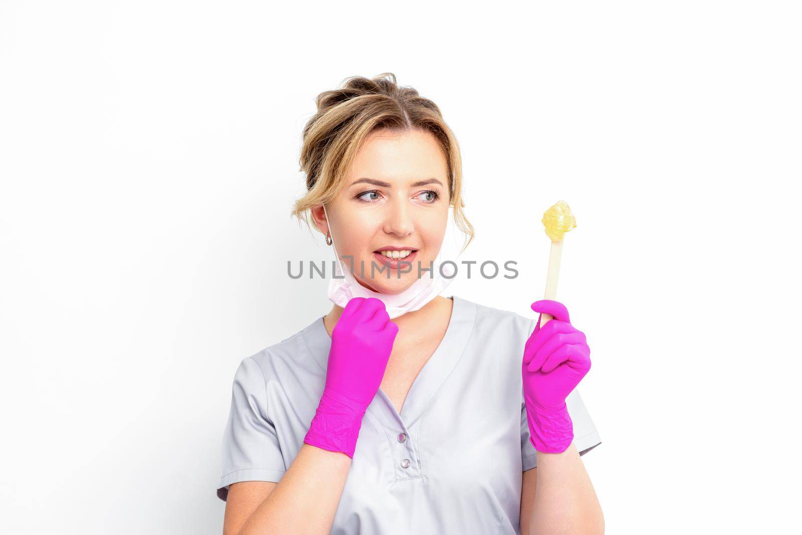 The master of sugar hair removal holds liquid yellow sugar paste, wax for depilation on a wooden stick on a white background. by okskukuruza