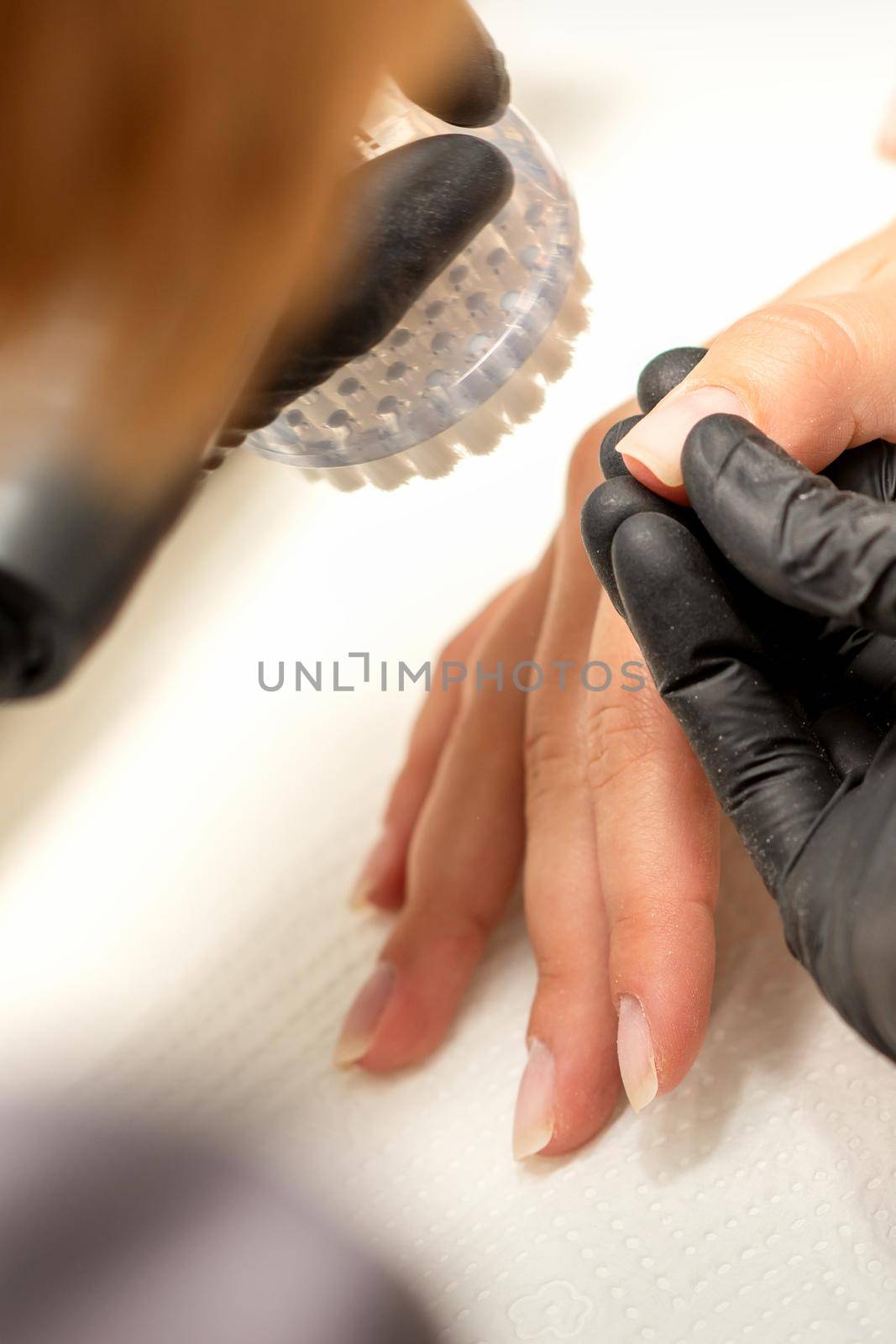 Hands of the manicure master removing dust from nails with a brush cleaning nails in a nail salon