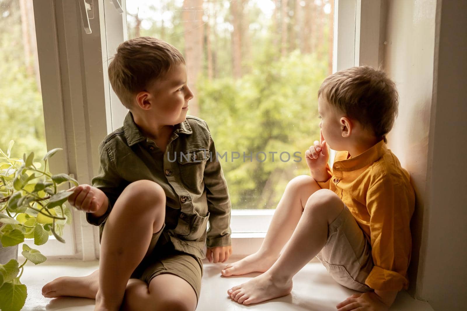 Children sitting on windowsill and waiting for someone comming. Two brothers, friends. Cute preschool kids alone at home. Boys are waiting for their mother or father. Loneliness. Busy parents