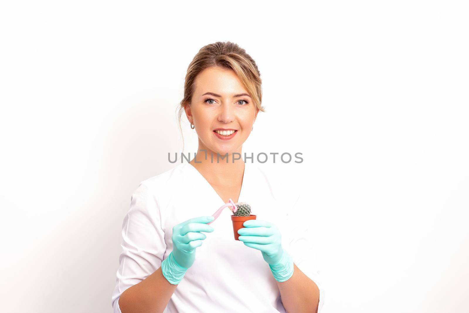 A smiling female beautician holds little green cactus with the razor in her hands. Hair removal concept