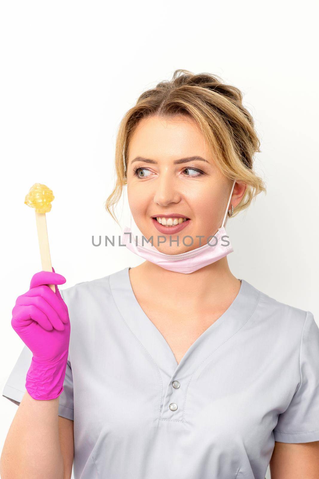 The master of sugar hair removal holds liquid yellow sugar paste, wax for depilation on a wooden stick on a white background. by okskukuruza