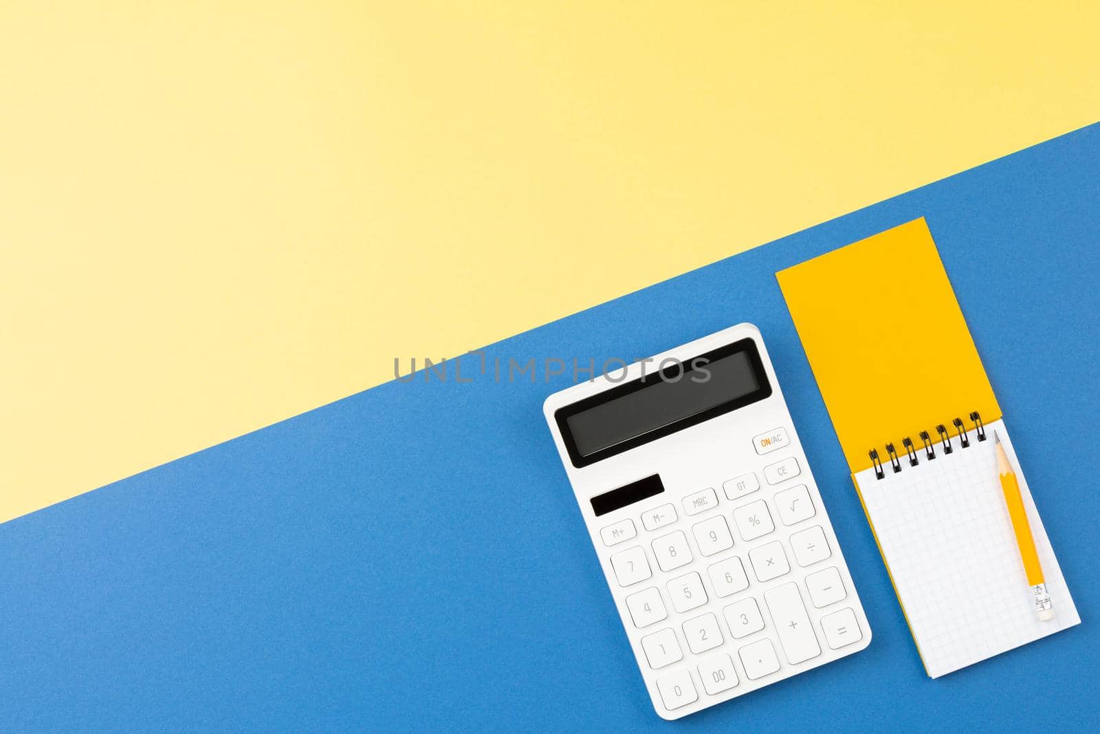 Calculator with a spiral notepad and pencil on two color background flat lay. Top view office desk concept.