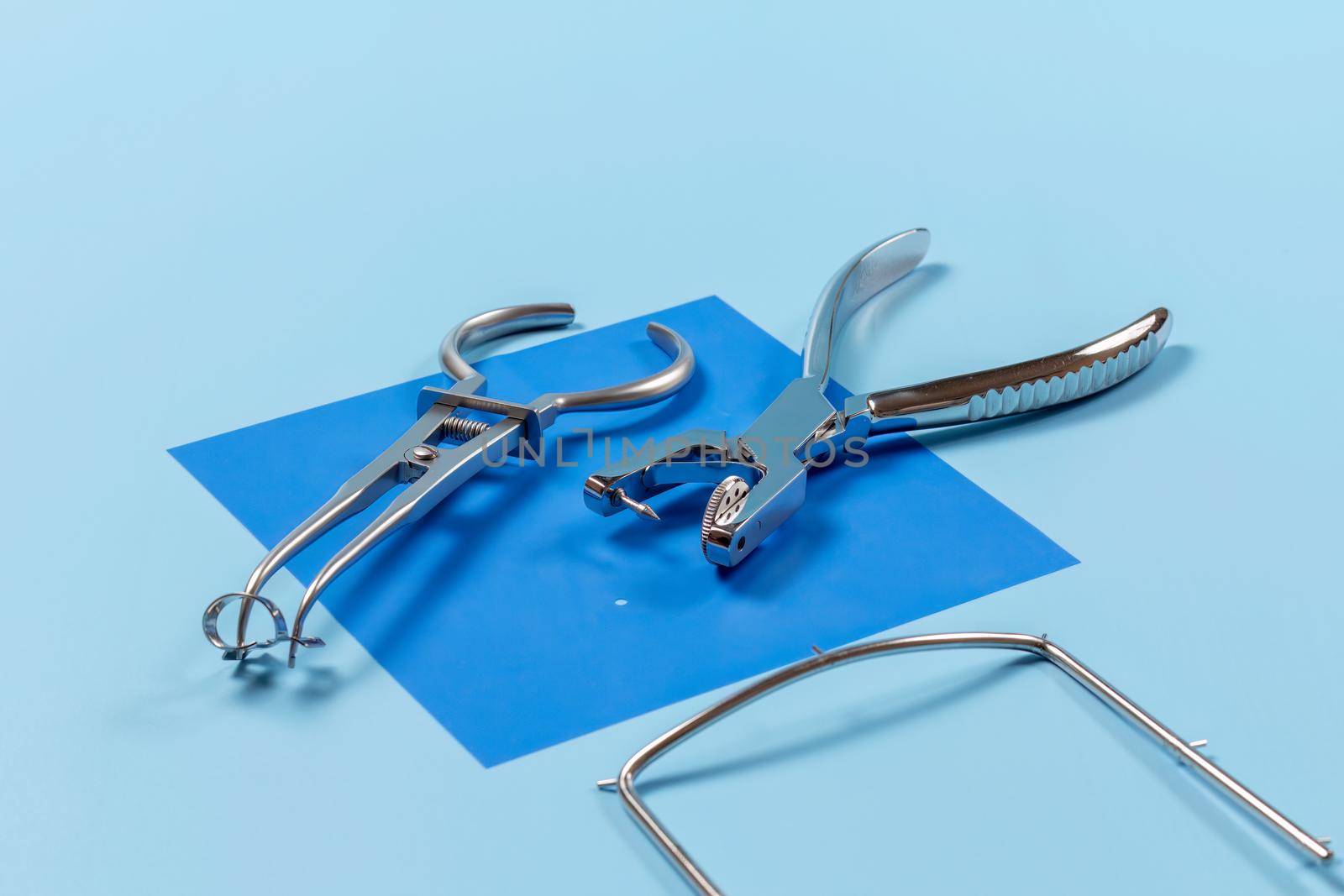 Dental hole punch, a rubber dam forceps with the clamp on the blue rubber dam and the metal frame. Medical tools concept.