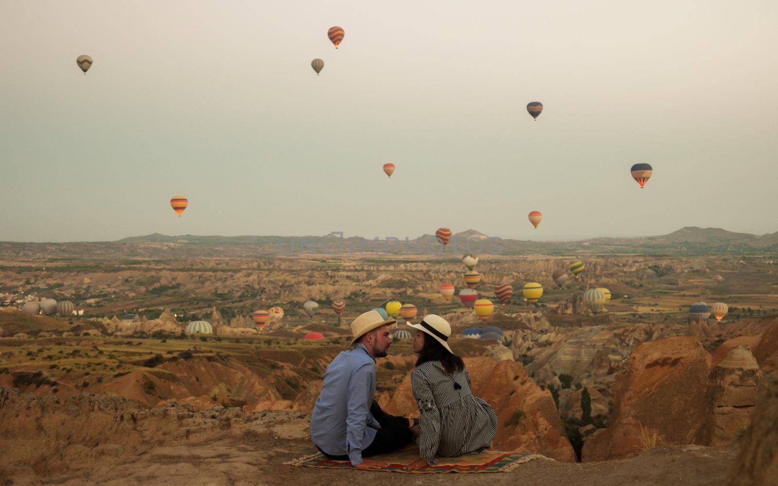 Kapadokya Cappadocia Turkey, a happy young couple during sunrise watching the hot air balloons of Kapadokya Cappadocia Turkey during vacation. Asian women and caucasian men on holiday in Turkey