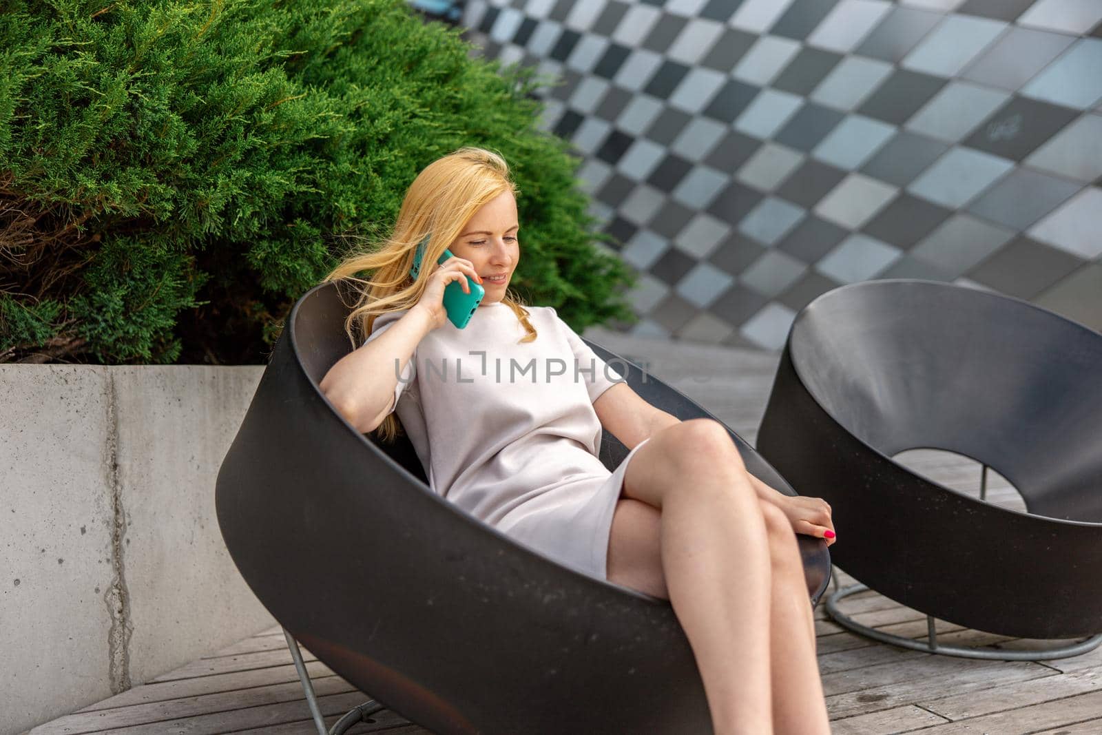 Young blond woman sittings outdoors in the city and making a call with her smartphone. Girl talking with friends with mobile phone. Leisure activity, communication. Conversation. Mobile technology. by creativebird