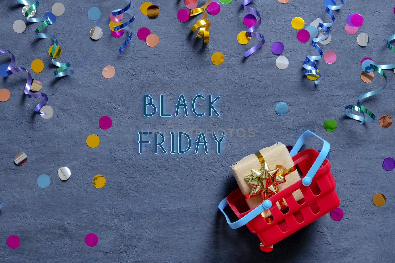 Black Friday tetx with shopping basket and festive tinsel flat lay on dark background. Top view by ssvimaliss