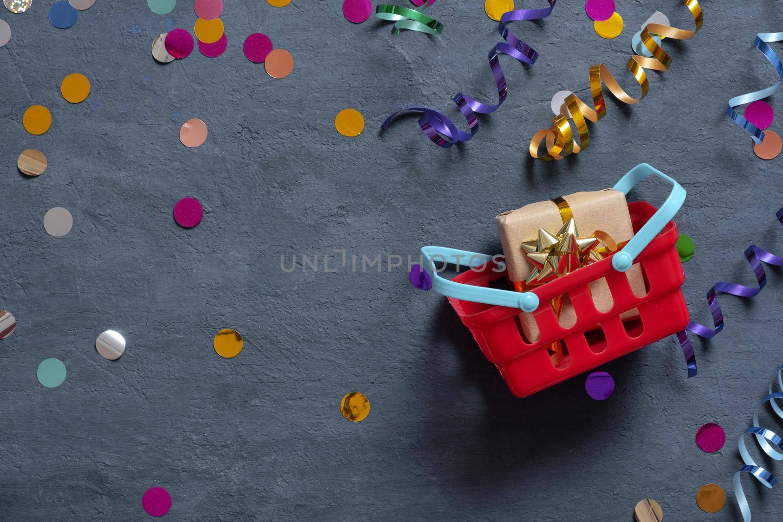 Shopping basket with gift box and festive tinsel flat lay on dark background. Top view by ssvimaliss