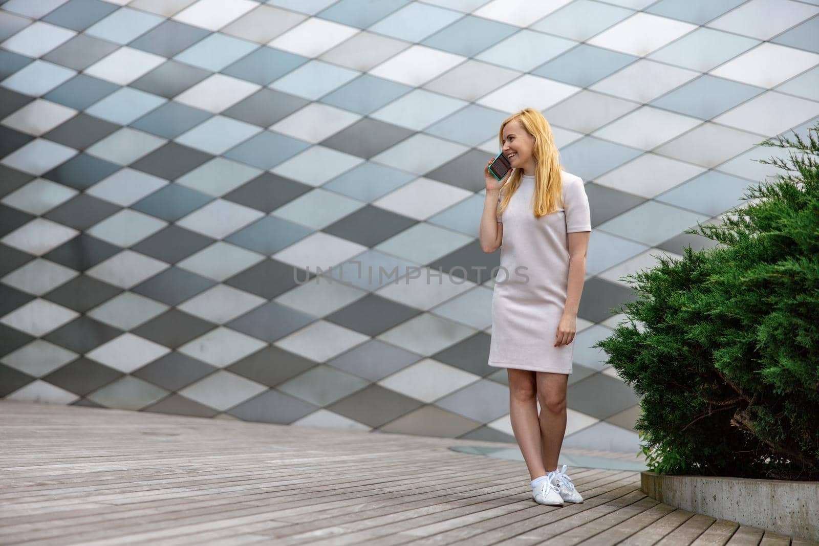 Young blond woman making a call with her smartphone. Girl talking with friends with mobile phone. Leisure activity, communication. Conversation. Mobile technology