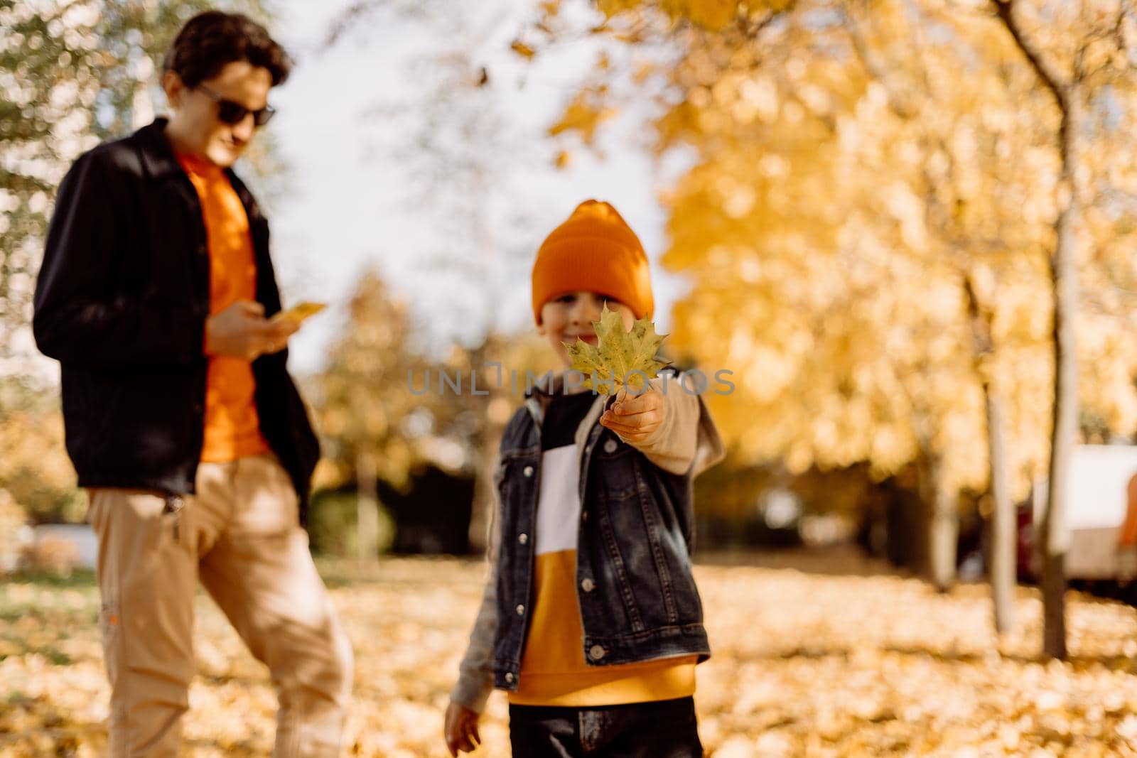 Father and son having fun in autumn park with fallen leaves, throwing up leaf. Child kid boy and his dad outdoors playing with maple leaves