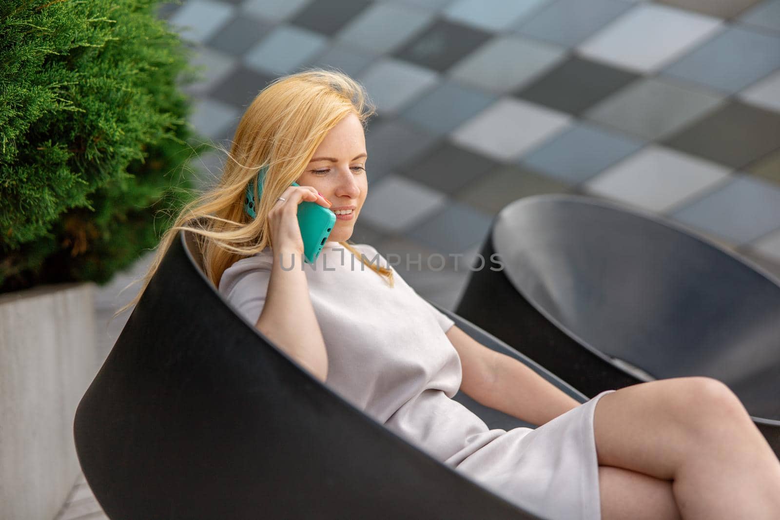 Young blond woman sittings outdoors in the city and making a call with her smartphone. Girl talking with friends with mobile phone. Leisure activity, communication. Conversation. Mobile technology. by creativebird