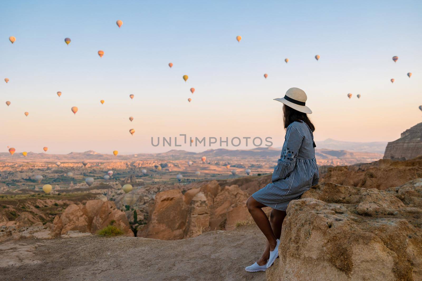 Asian women watching the sunset in Cappadocia with hot air balloons in the sky during sunrise in Cappadocia Turkey. Kapadokya Gorem. Happy mid age women in a hot air balloon