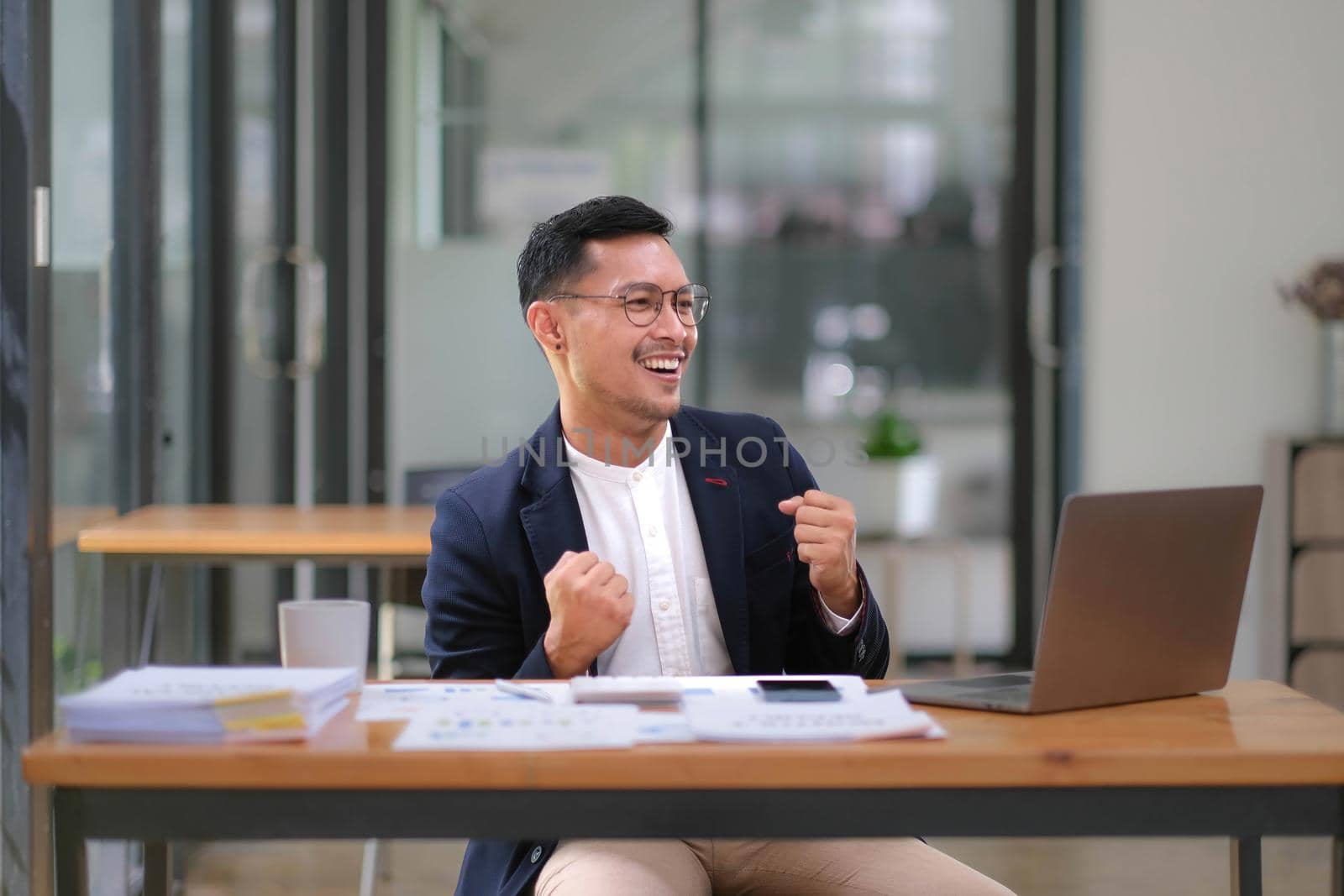 Portrait of an Asian male business owner standing with a computer showing happiness after a successful investment. by wichayada