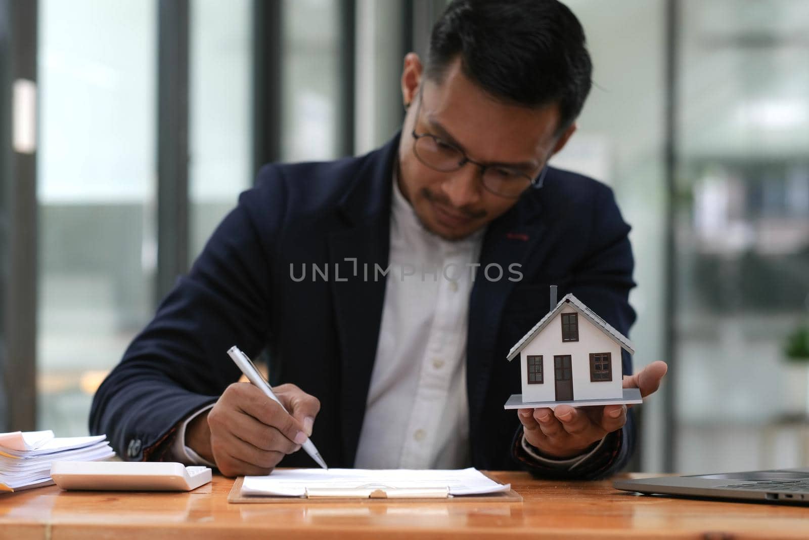 Business man hands holding modern house, House model with agent and customer discussing for contract to buy, get insurance or loan mortgage crisis real estate or property. by wichayada