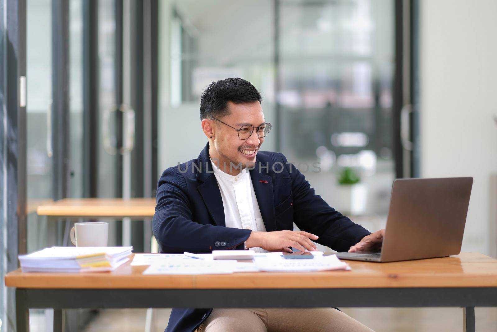 Professional and successful adult Asian businessman or male boss in formal suit is working at his desk, using digital tablet and checking the report..