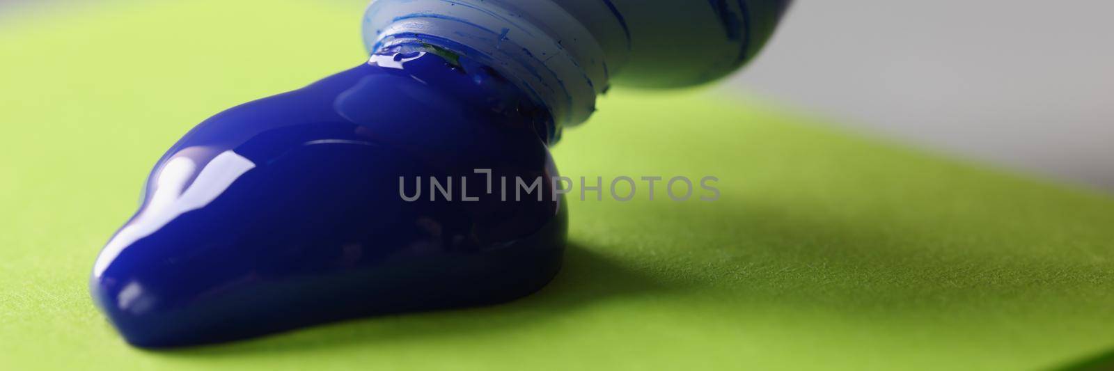 Close-up of man artist squeeze paint out of tube, bright blue colour on green paper. Tool for further creative masterpiece. Art, creativity, hobby concept