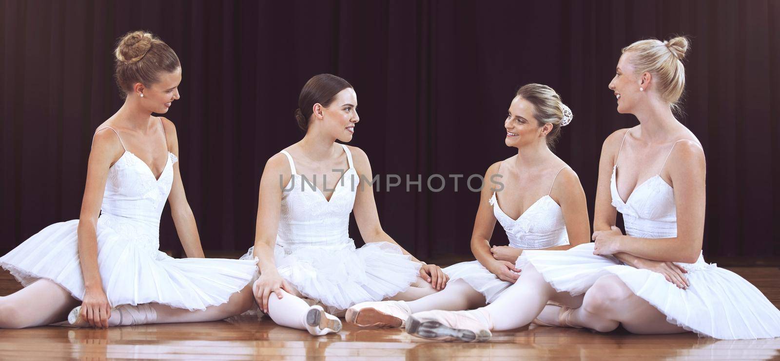 Ballet, art and women resting after training on a theater stage for a classical performance. Creative dance, elegant and dancers sitting on the floor and talking after practice to relax and rest