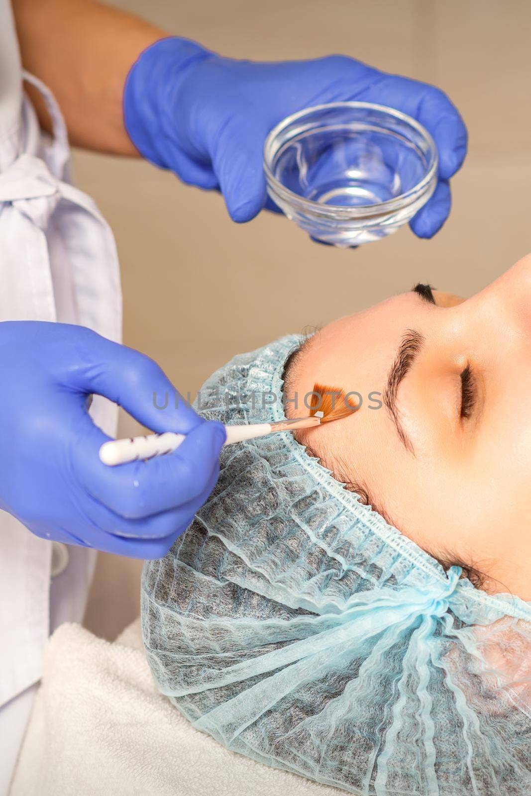 Young white woman getting acid organic retinol peel face skin with the brush in a beauty clinic. by okskukuruza