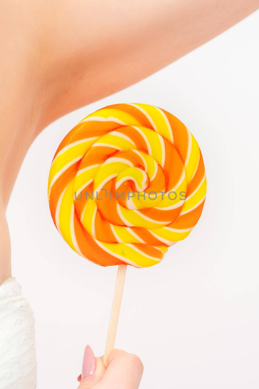 Waxing, depilation concept. A young female holds a round lollipop near her armpit on white background