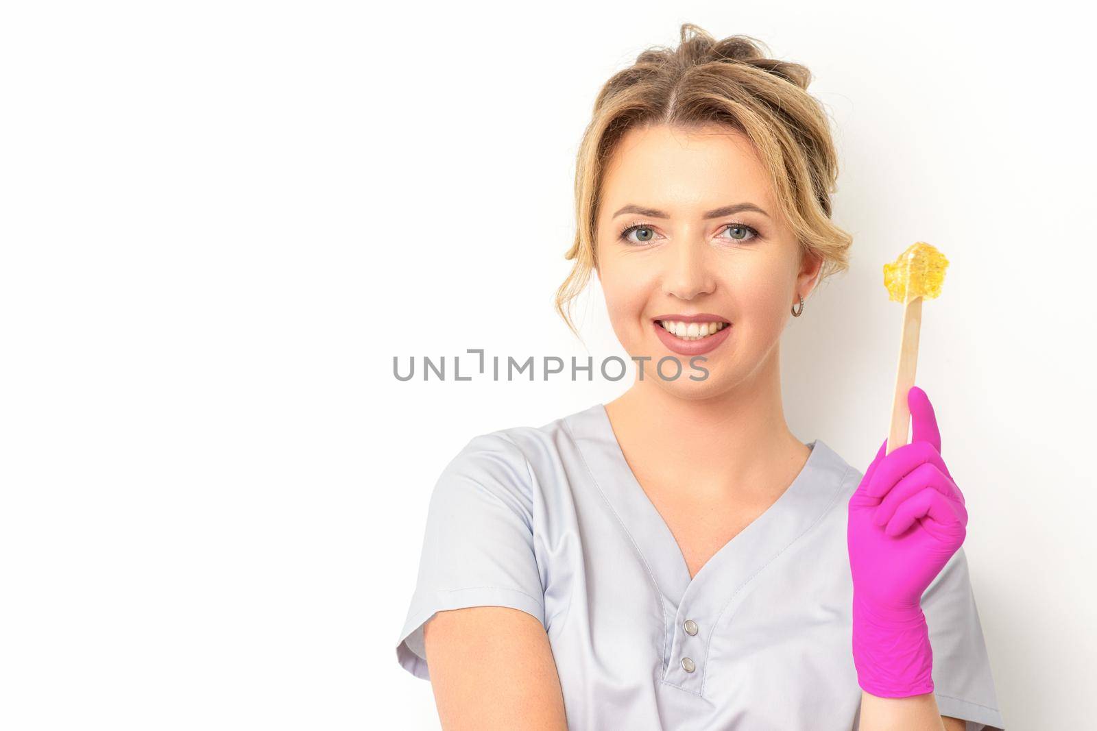 The master of sugar hair removal holds liquid yellow sugar paste, wax for depilation on a wooden stick on a white background