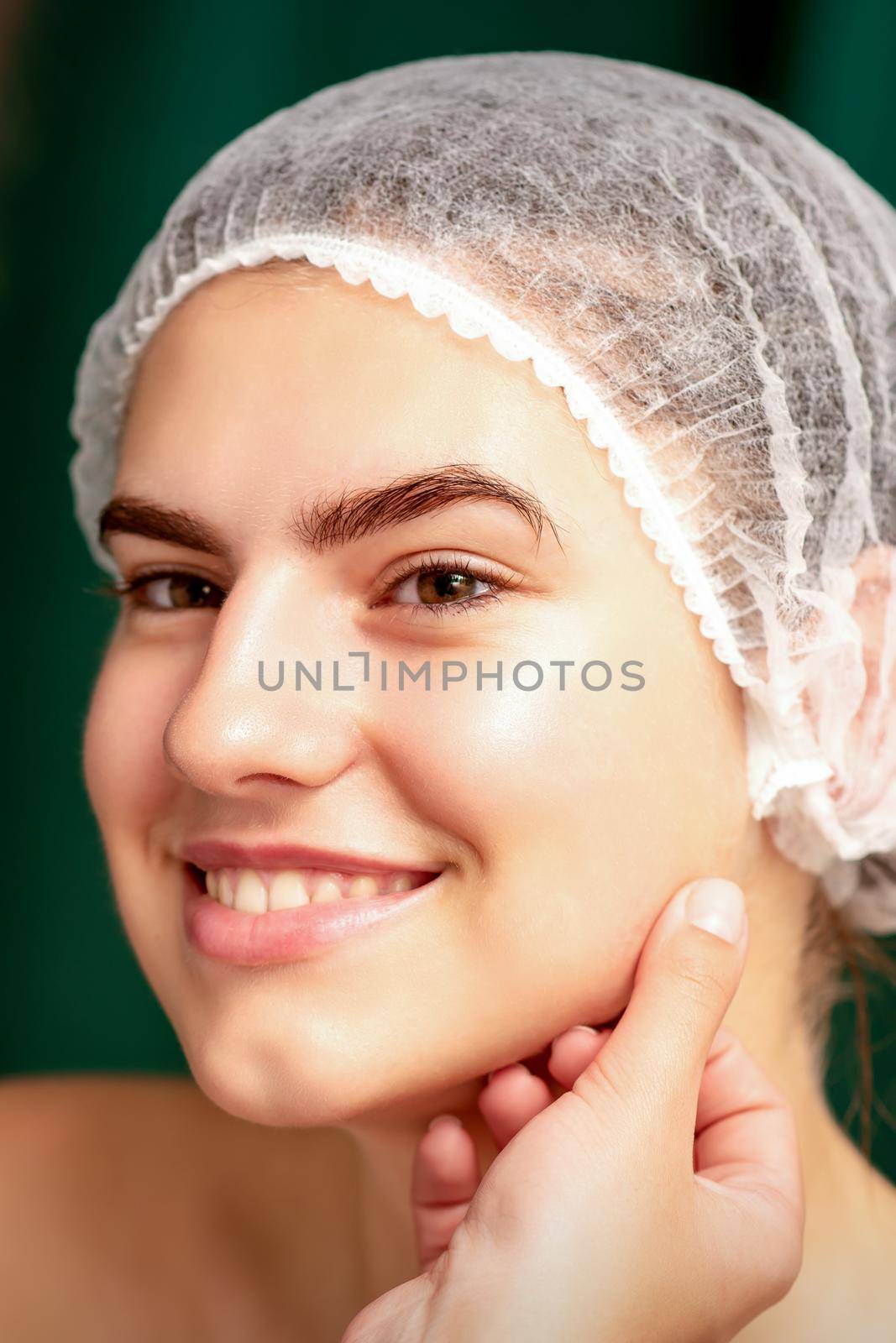 Plastic surgery and beauty concept. Professional cosmetician examining and touching the face of the beautiful young caucasian smiling woman in a clinic of esthetic cosmetology