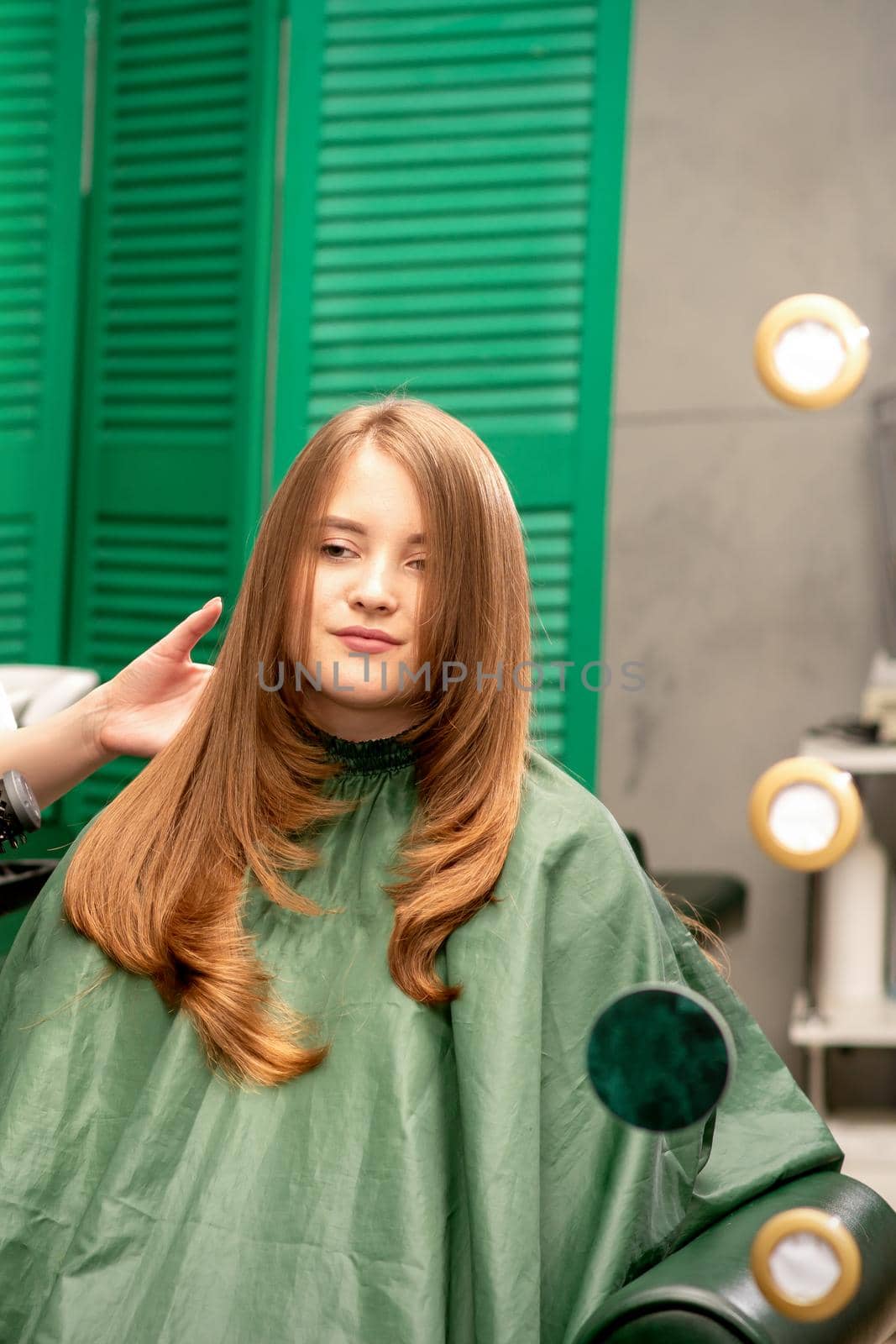 Professional hair care. Young female red-haired with long hair receiving hairstyling in a beauty salon.