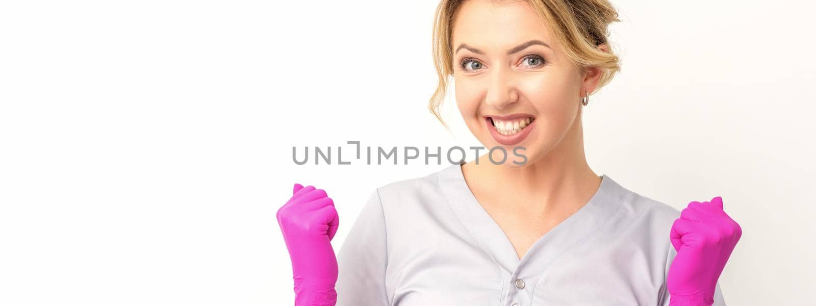 Happy caucasian woman doctor wearing pink gloves celebrates and raising fists on white background