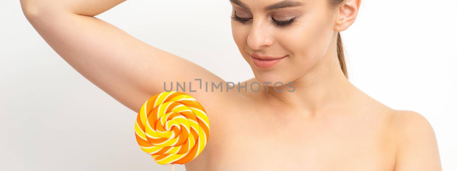 Waxing, depilation concept. The beautiful young caucasian woman covers her armpit with a lollipop on white background