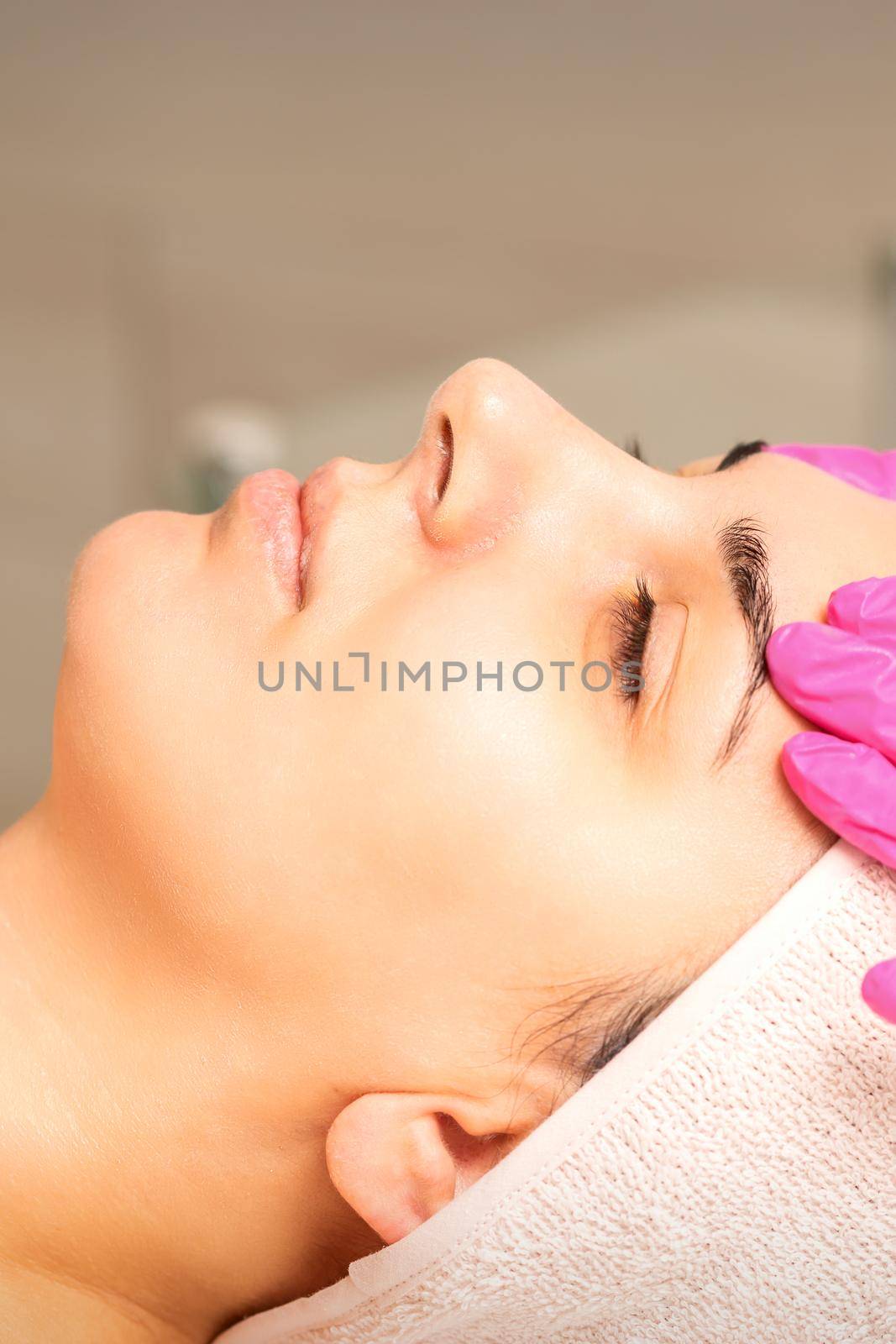 Cosmetologist with gloved hands applies a moisturizing mask with peeling cream on the female face. Facial cosmetology treatment. Procedures for facial care