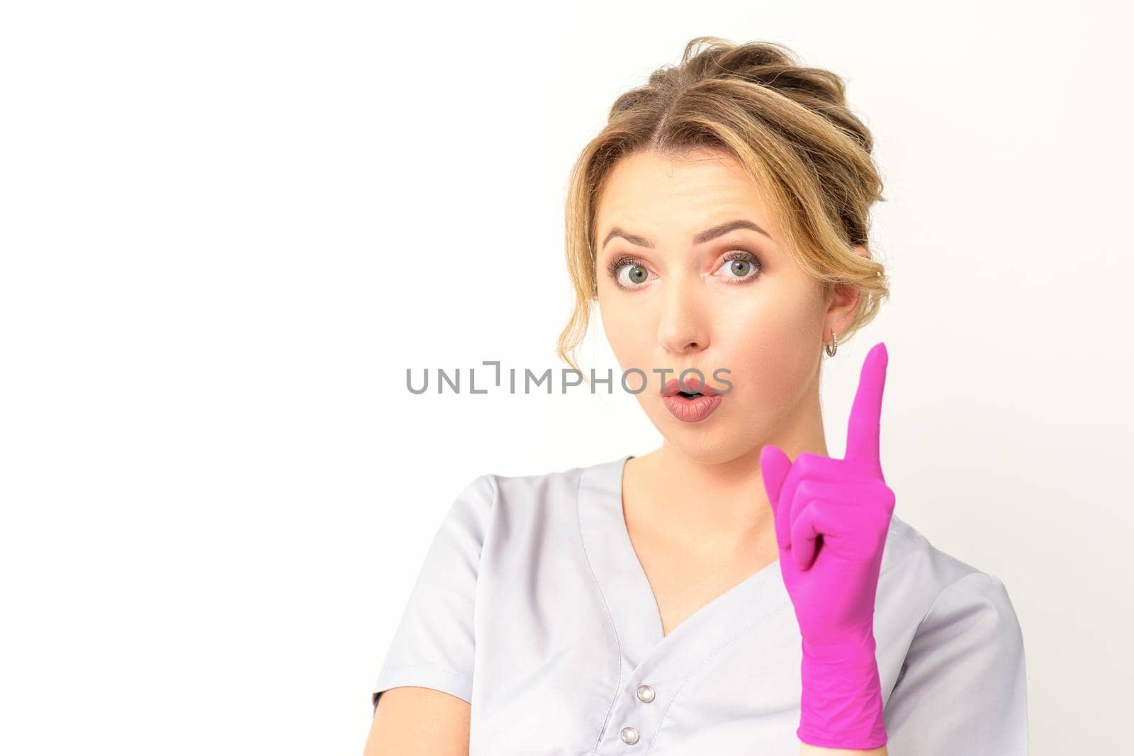 Young caucasian woman doctor wearing pink gloves keeping index finger pointed upwards making a gesture with index finger. I have an idea