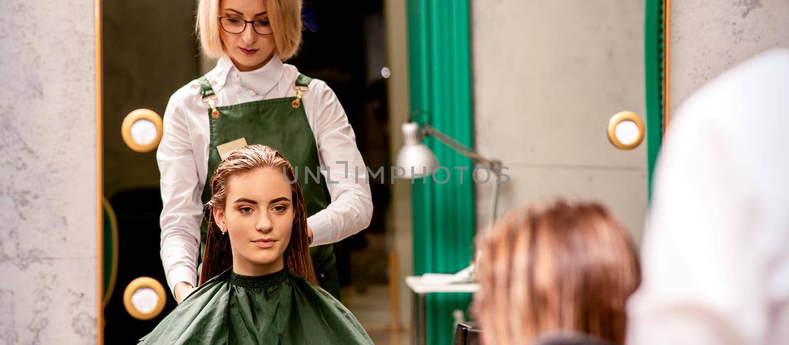 Professional hair care. Beautiful young caucasian brunette woman with long hair receiving hairstyling in a beauty salon. by okskukuruza