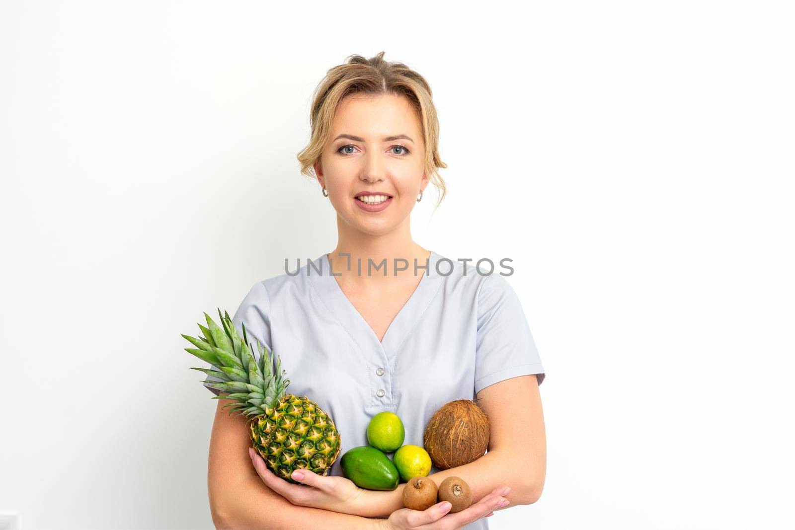 Portrait of a young caucasian smiling female nutritionist with different fruits in her hands over white background. by okskukuruza
