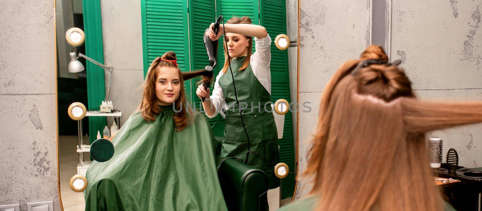 The hairdresser is drying long brown hair with a hairdryer and round brush in a beauty salon