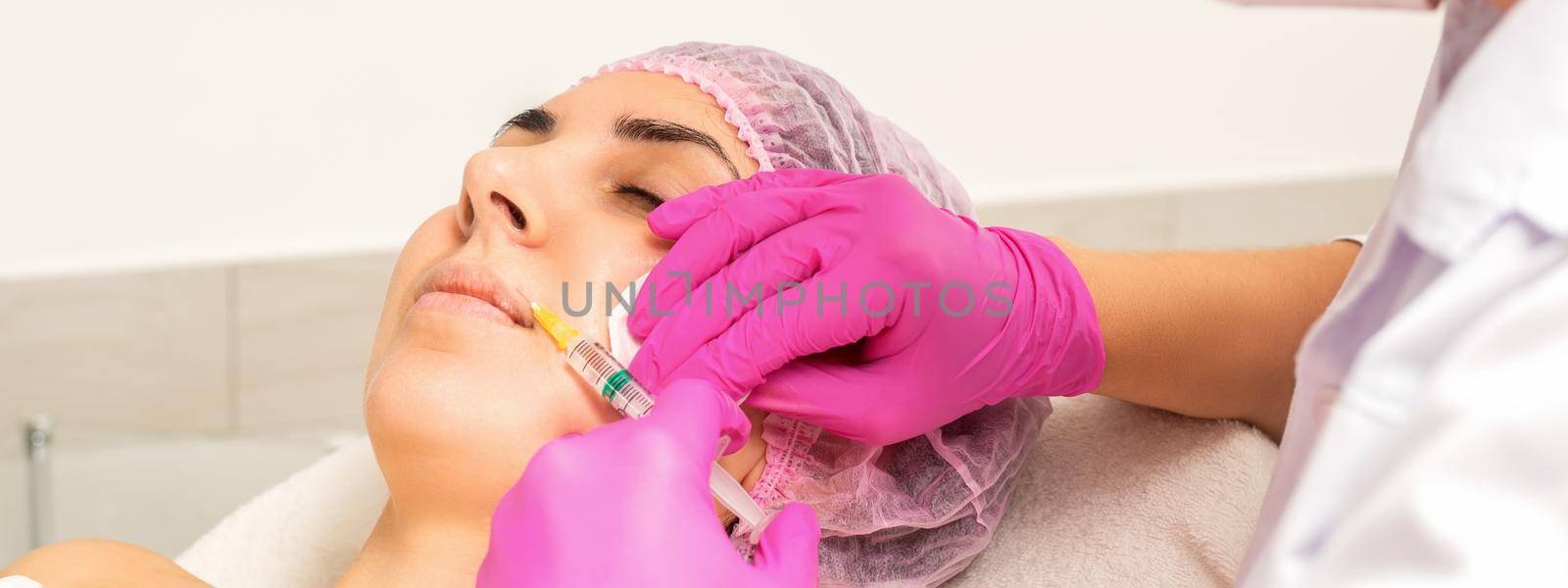 Young caucasian woman getting botox injection with hyaluronic acid in the lips at a beauty clinic. by okskukuruza