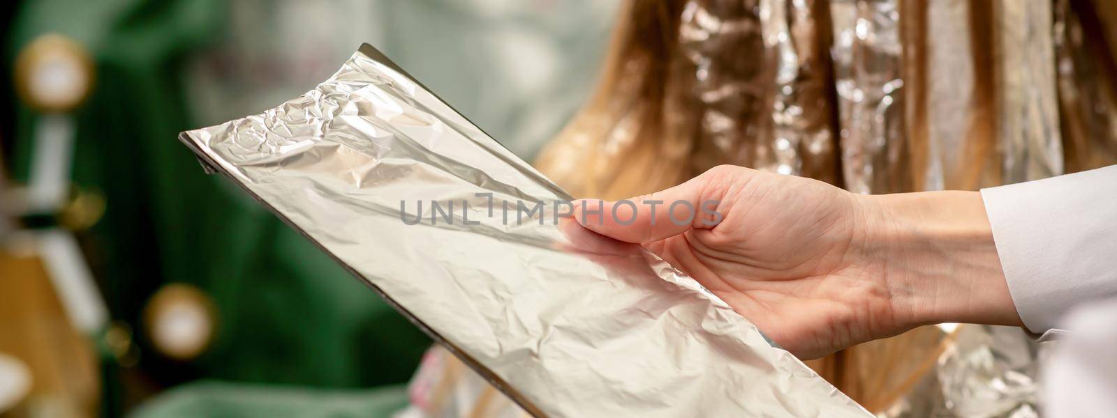 Hairdresser's Hands Holding Foil Sheet For Hair Dye In Beauty Salon
