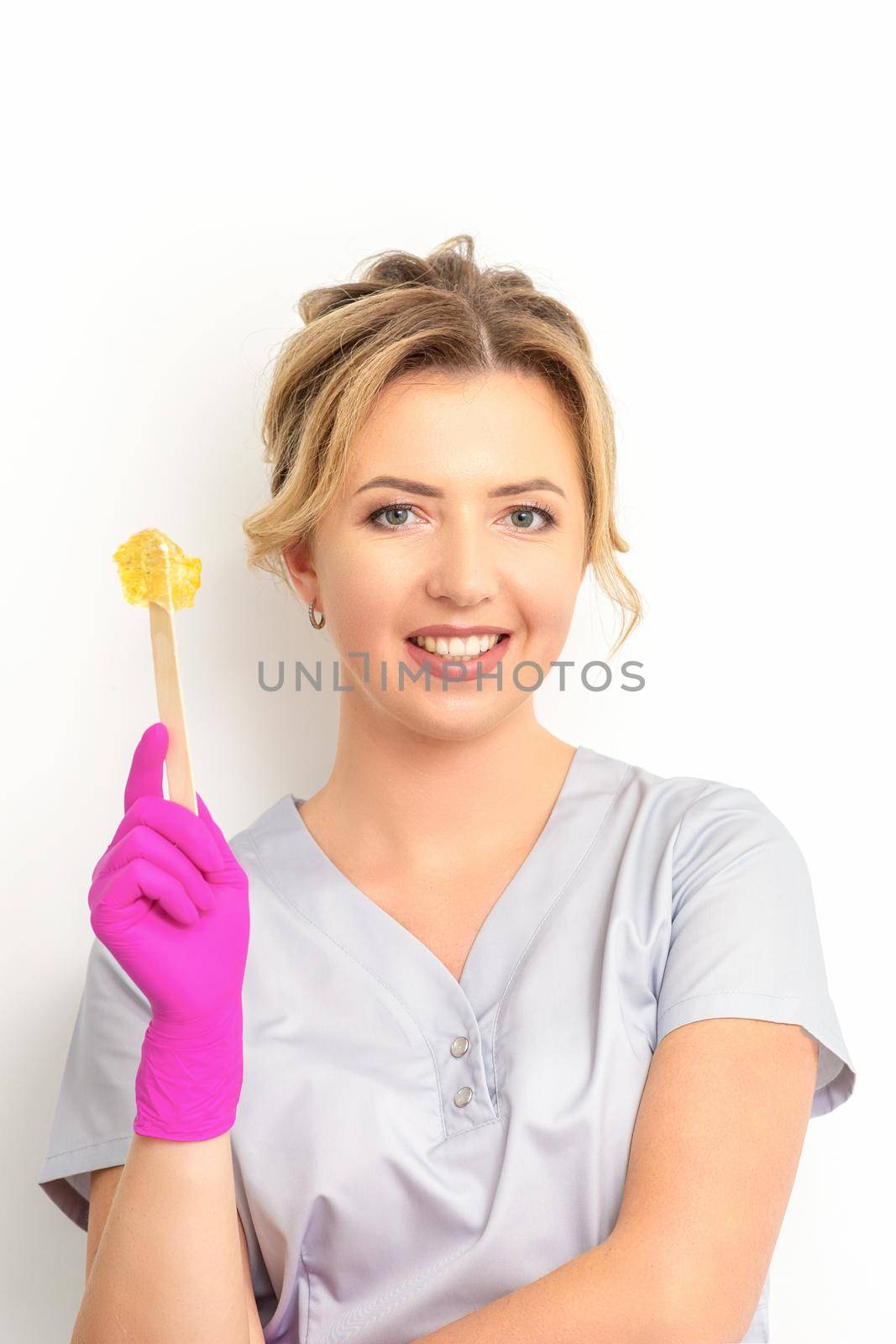 The master of sugar hair removal holds liquid yellow sugar paste, wax for depilation on a wooden stick on a white background