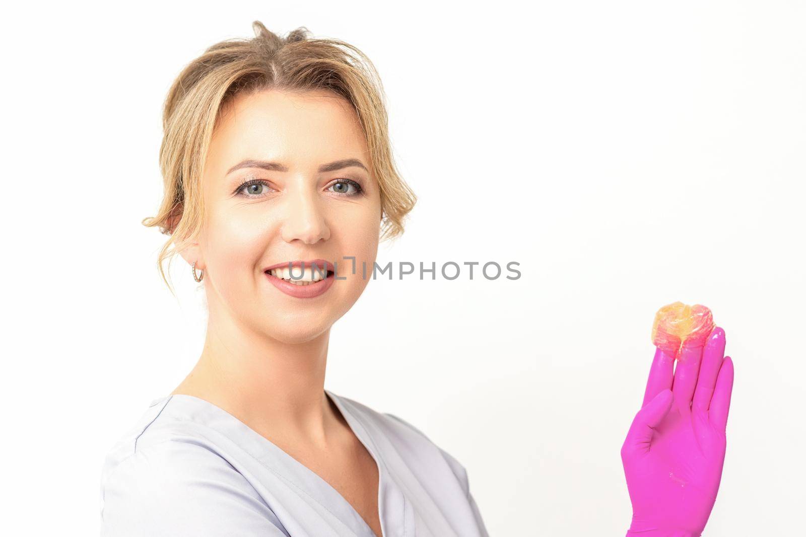 Young caucasian smiling female beautician holding wax for depilation over white background. Yellow sugar paste in hands master of depilation. Epilation concept. by okskukuruza