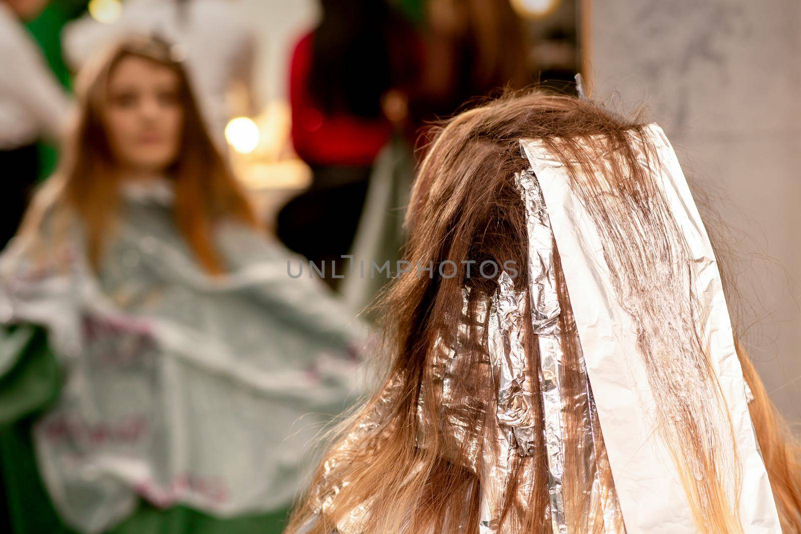 Beautiful young caucasian woman with foil in her hair while dyeing her hair sitting in a beauty salon