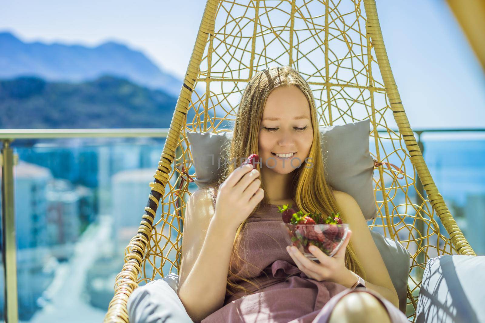 Portrait of gorgeous woman wearing beautiful dress sitting in a patio and eating strawberry.