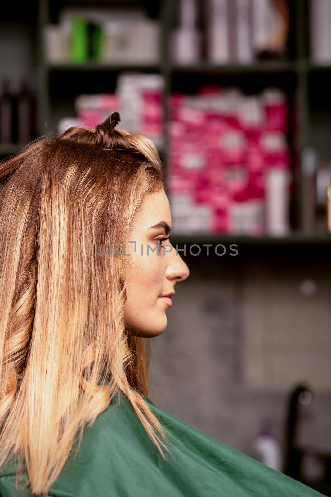 Professional hair care. Beautiful young caucasian blonde woman with long hair receiving hairstyling in a beauty salon. by okskukuruza