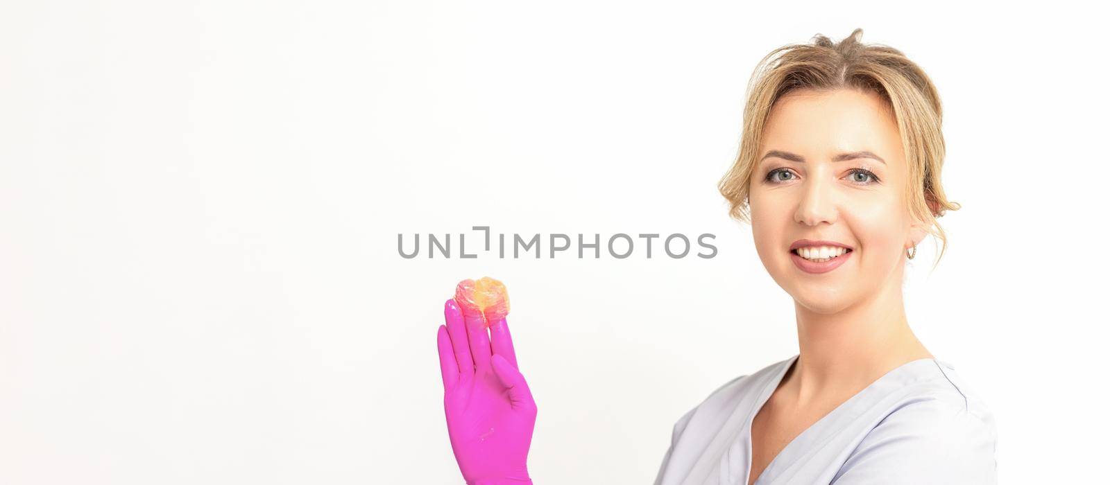 Young caucasian smiling female beautician holding wax for depilation over white background. Yellow sugar paste in hands master of depilation. Epilation concept