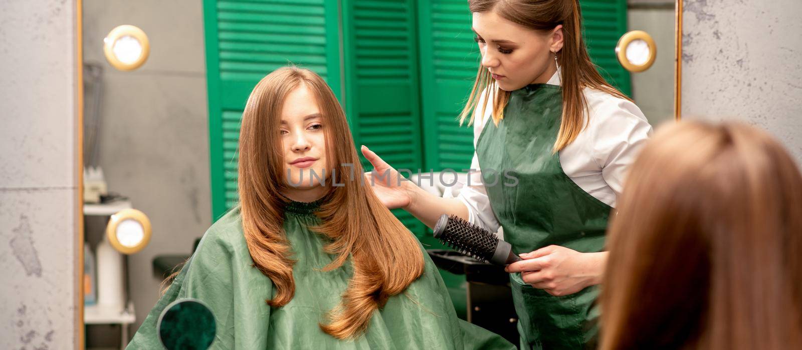Professional hair care. Young female red-haired with long hair receiving hairstyling in a beauty salon by okskukuruza